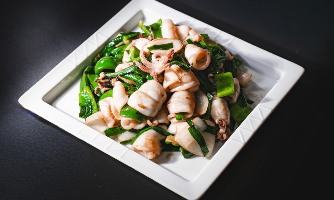 Stir-fried squid with green pepper and scallion on a white plate