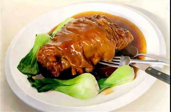 Whole braised pork hock in glossy red sauce with baby bok choy
